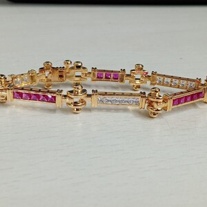 May include: A gold-toned link bracelet featuring alternating rectangular segments set with princess-cut pink and clear white stones. The metal frame has a polished finish with decorative rounded connectors between each stone-set section.