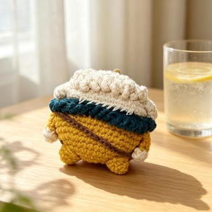 May include: A crochet case for wireless earbuds featuring a yellow base, a dark teal middle band, and a textured white top section. The design includes a thin brown strap detail across the yellow portion and small white accents on the sides.
