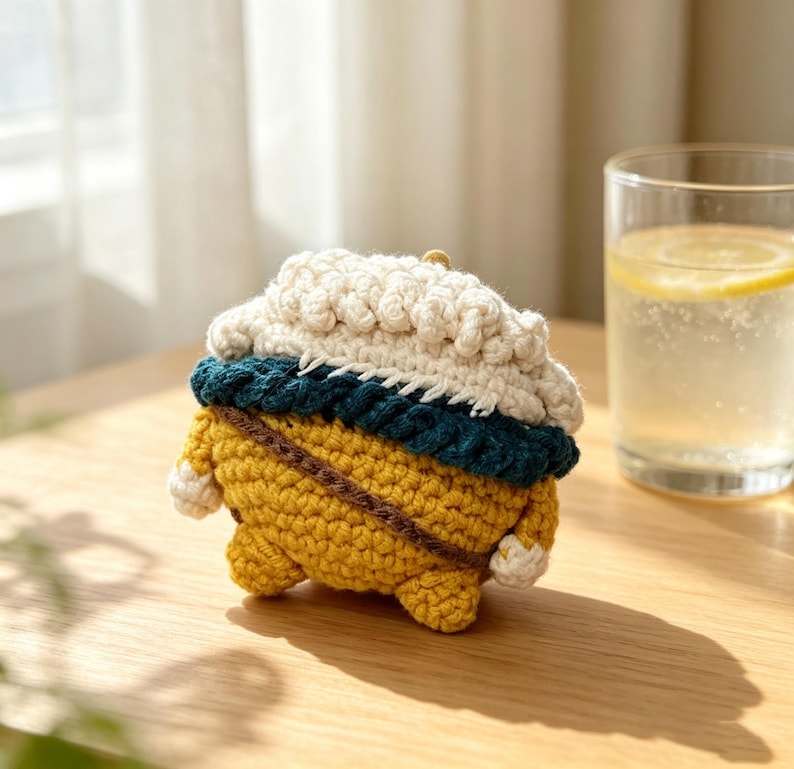 May include: A crochet case for wireless earbuds featuring a yellow base, a dark teal middle band, and a textured white top section. The design includes a thin brown strap detail across the yellow portion and small white accents on the sides.