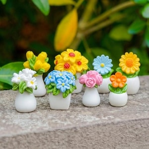 May include: A collection of miniature flower arrangements in white ceramic vases. The flowers are in various colors, including yellow, blue, pink, and orange. The arrangements are set on a stone surface with a blurred green background.