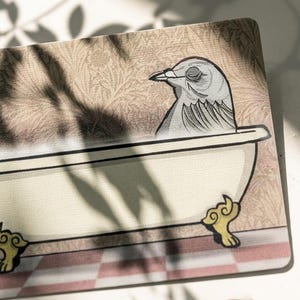 Pode incluir: Tapete decorativo com uma ilustração de desenho animado de um pássaro cinza relaxando em uma banheira branca. O tapete tem um fundo bege com um padrão floral e uma borda xadrez vermelha e branca.