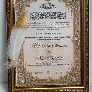 May include: A framed Islamic marriage certificate with gold ornate borders and crystal accents. The text includes names Mohamed Sameer and Nur Ashifah, dated 03 August 2026. A white and gold feather quill pen is attached to the left side of the frame.