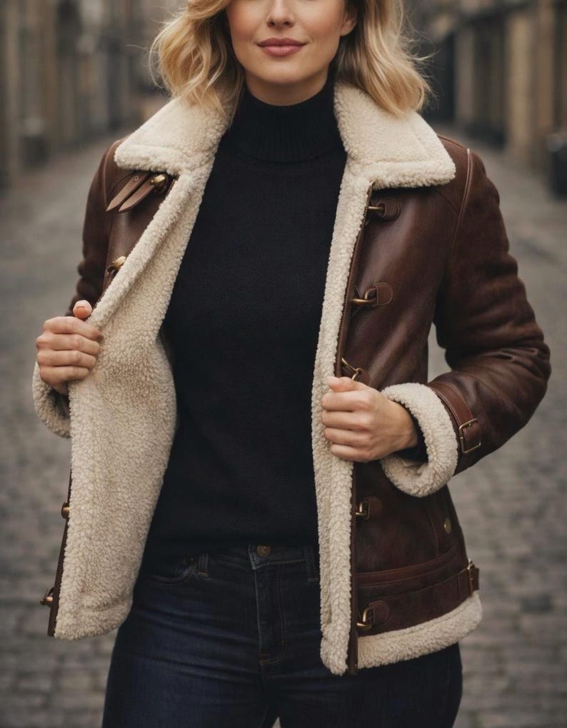 Puede incluir: Chaqueta de cuero marr&oacute;n con forro y cuello de borrego color crema. La chaqueta tiene cierres de palanca y detalles de cintur&oacute;n con hebilla en los pu&ntilde;os. Se lleva un cuello alto negro y vaqueros azul oscuro.