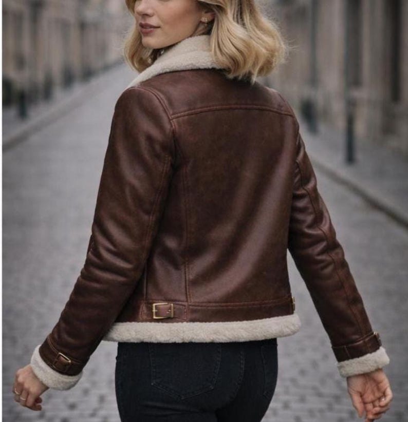 Puede incluir: Chaqueta de cuero marr&oacute;n con cuello y forro de borreguillo color crema. La chaqueta tiene un estilo aviador cl&aacute;sico con cintura y pu&ntilde;os abrochados. La modelo lleva vaqueros negros.