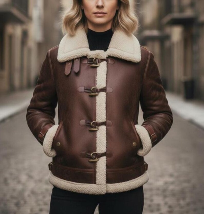 Puede incluir: Chaqueta de cuero marr&oacute;n con cuello y forro de borrego color crema. La chaqueta presenta cierres de palanca y ribete de borrego en los pu&ntilde;os y bolsillos. Una prenda de abrigo elegante.