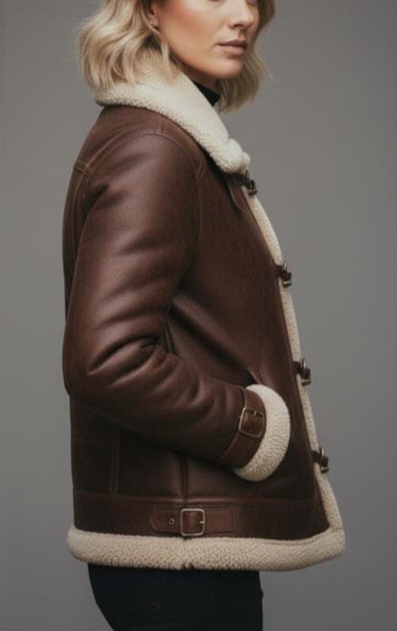 Puede incluir: Chaqueta de cuero marr&oacute;n con forro y ribete de borreguillo color crema. La chaqueta presenta un dise&ntilde;o cl&aacute;sico con cuello de solapa, detalles de hebillas y una est&eacute;tica c&aacute;lida y acogedora. La chaqueta tiene un aspecto acogedor y listo para el invierno.