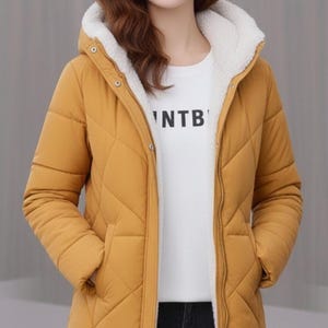 May include: Mustard yellow quilted puffer jacket with a white fleece-lined hood and interior. The jacket has a zip closure, pockets, and a white t-shirt underneath with the text 'NTB'.