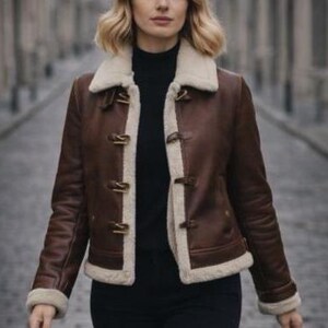 Puede incluir: Chaqueta de cuero marr&oacute;n con forro y ribete de borreguillo color crema. La chaqueta presenta cierres de palanca y un cuello de borreguillo. Las mangas tienen pu&ntilde;os de borreguillo. La chaqueta se lleva sobre un cuello alto negro.