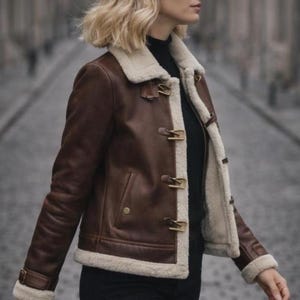 Puede incluir: Chaqueta de cuero marr&oacute;n con forro y ribete de borreguillo color crema. La chaqueta presenta cierres de palanca y un dise&ntilde;o cl&aacute;sico. Las mangas tienen un detalle de hebilla en la mu&ntilde;eca. Una elegante prenda de abrigo.