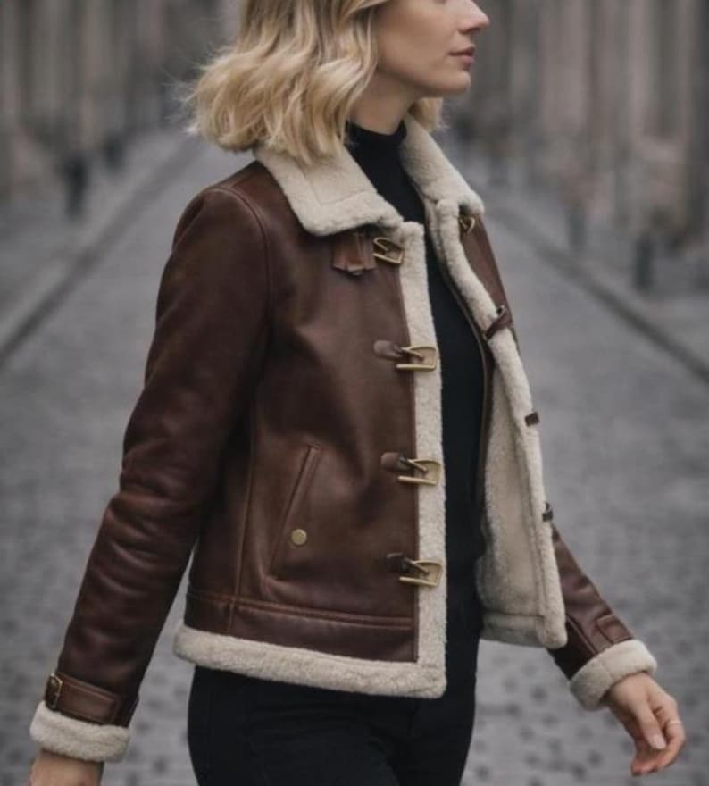 Puede incluir: Chaqueta de cuero marr&oacute;n con forro y ribete de borreguillo color crema. La chaqueta presenta cierres de palanca y un dise&ntilde;o cl&aacute;sico. Las mangas tienen un detalle de hebilla en la mu&ntilde;eca. Una elegante prenda de abrigo.