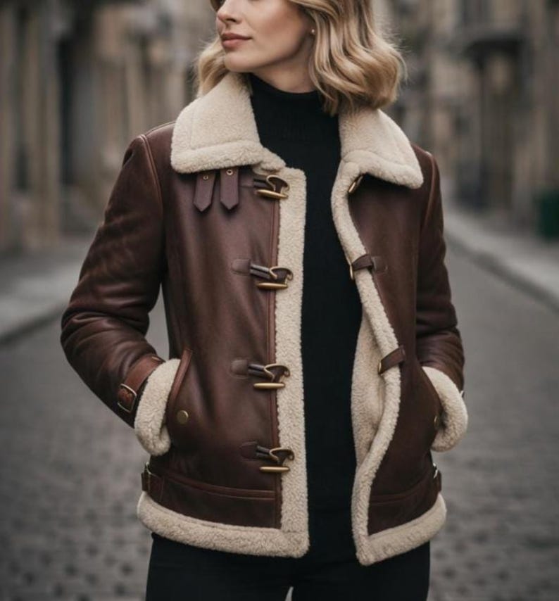 Puede incluir: Chaqueta de cuero marr&oacute;n con forro y cuello de borreguillo color crema. La chaqueta presenta cierres de palanca y un estilo aviador cl&aacute;sico. La modelo lleva un cuello alto negro. La chaqueta tiene dos bolsillos delanteros.