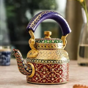 May include: A decorative metal teapot featuring a vibrant hand-painted design with a deep red base, intricate gold floral patterns, and a dark blue handle. The lid and spout are adorned with colorful geometric accents and small embedded crystals.