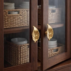 May include: A dark wood cabinet with glass doors and gold leaf-shaped handles. Inside, woven baskets hold stacks of white plates and bowls. The cabinet is a storage solution for a kitchen or dining area.