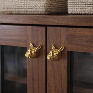 May include: A dark wood cabinet with two gold rhino head door pulls. The cabinet doors are closed. Two woven baskets sit on top of the cabinet.