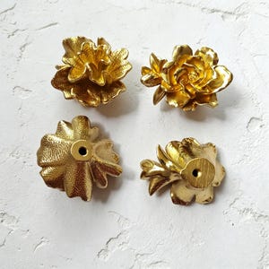 May include: Four gold-colored flower-shaped cabinet knobs. The knobs are made of metal and have a detailed floral design. The knobs are shown from different angles, with the back of the knobs showing the screw hole.
