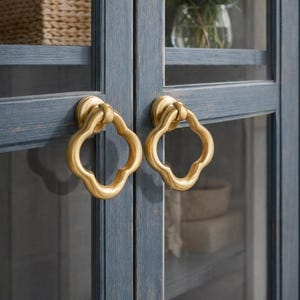 Peut inclure: Gros plan sur une armoire bleue avec des portes vitrées et des poignées décoratives dorées. Les portes de l'armoire sont fermées, et l'intérieur est partiellement visible, avec des étagères et un vase de fleurs.