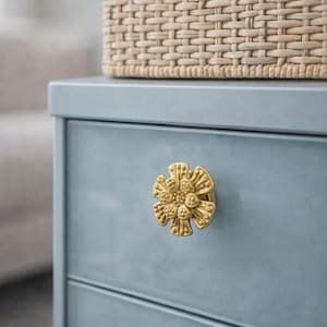 May include: A close-up of a light blue dresser with a gold flower-shaped knob. A woven basket sits on top of the dresser. The knob is a decorative accent.