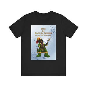 May include: A black t-shirt featuring a graphic of a cat dressed in a green suit, star-adorned hat, and sunglasses, playing a bass guitar. The text reads PUSS IN BOOT-SY COLLINS THE CAT THAT LICKED BASE against a light blue background with musical notes.