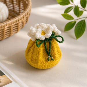 May include: A handmade yellow crochet pouch with a cluster of white and yellow crochet flowers on top. The pouch is tied with a green cord and has small beads. The item is likely a small bag or decorative item.