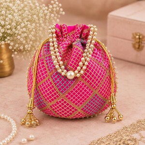 Peut inclure: Une pochette à cordon rose vif ornée d'un motif à grille dorée et de touches bleues. Le sac possède une anse composée de deux rangs de fausses perles blanches et des pompons en métal doré suspendus sur les côtés avec de petites perles dorées.