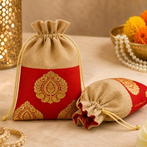 May include: Two drawstring gift bags. The bags are made of tan burlap with a red panel featuring a gold floral design. The bags have a drawstring closure and are suitable for small gifts or favors.