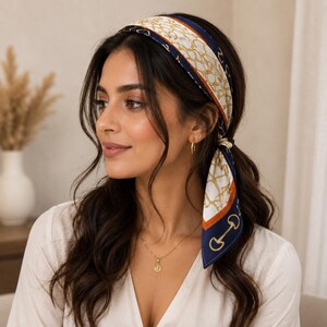 May include: A square hair scarf tied around the head, featuring a white background with a gold chain-link pattern, a navy blue border, and orange accents. The fabric displays a repeating equestrian-inspired bit motif along the dark blue edges.