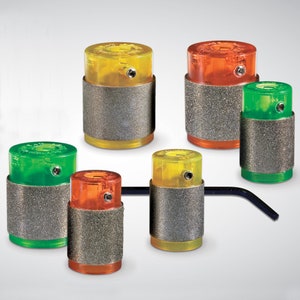 May include: Assortment of six colorful, cylindrical, grinding tools with a textured gray surface. Each tool has a clear top and a colored base. The tools are arranged in a row on a gray background.