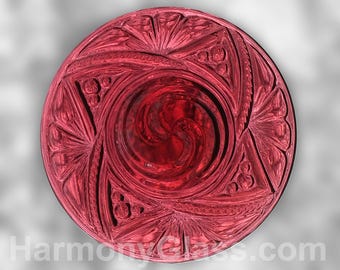 Puede incluir: Un plato de vidrio rojo oscuro con un diseño en relieve en espiral. El plato tiene un centro elevado y un borde decorativo.