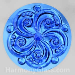 May include: A blue glass tile with a decorative, swirling pattern. The tile has a shiny, metallic finish.