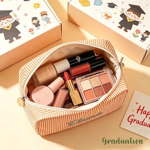 Könnte beinhalten: Eine gestreifte Kosmetiktasche gefüllt mit Make-up-Produkten, darunter Lippenstifte, Lidschatten und Foundation. Die Tasche ist geöffnet und zeigt den Inhalt. Zwei Schachteln mit Illustrationen zum Thema Abschlussfeier sind im Hintergrund.