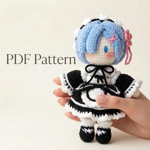 Könnte beinhalten: Handgefertigte Häkelpuppe mit blauen Haaren, einem schwarz-weißen Kleid und einer rosa Schleife. Die Puppe hat ein süßes Gesicht mit rosigen Wangen und blauen Augen. Der Text "PDF Pattern" ist im Bild zu sehen.