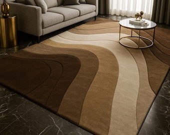Può includere: Un grande tappeto rettangolare con un motivo a onde nei toni del marrone, beige e crema. Il tappeto è posizionato su un pavimento scuro e lucido, di fronte a un divano chiaro e un tavolino rotondo.