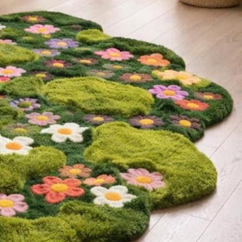 May include: A flower-shaped rug with a green, textured base resembling grass. The rug features crocheted flowers in pink, orange, white, and purple. The design creates a vibrant, garden-like appearance, perfect for a child's room or living space.