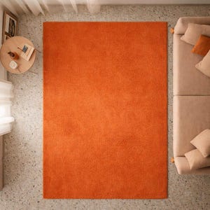 Könnte beinhalten: Draufsicht auf einen großen, rechteckigen orangefarbenen Teppich. Der Teppich ist der Mittelpunkt, mit einer weichen Textur und lebendigen Farbe. Rechts befindet sich ein beiges Sofa mit Kissen, links ein kleiner runder Tisch.