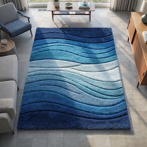 May include: A large, rectangular area rug with a wave-like pattern in shades of blue. The rug's design features a gradient of blues, from deep navy to light turquoise, creating a textured, plush appearance. The rug is placed in a living room setting.