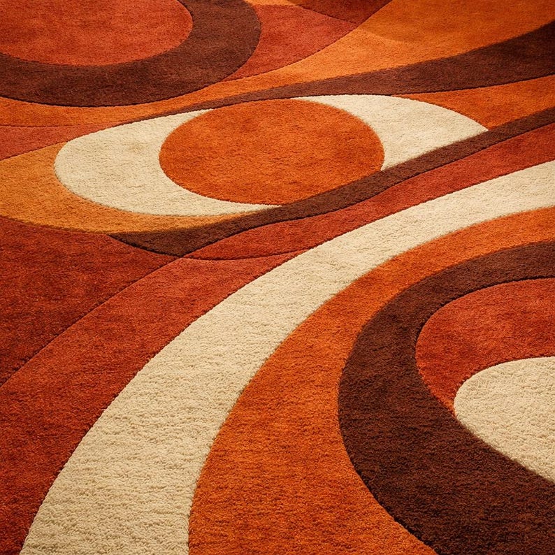 May include: A close-up of a retro-style rug with a swirling pattern. The rug features a combination of warm colors, including shades of orange, brown, and cream. The design is composed of curved lines and circular shapes, creating a textured, eye-catching surface.