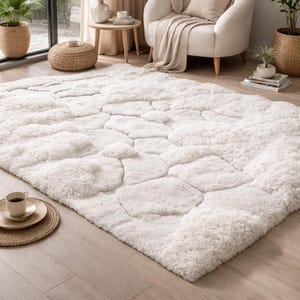 May include: A large, white, textured area rug with a pebble-like design. The rug is made of a soft, plush material and is placed on a light-colored wooden floor. The rug adds a cozy and inviting feel to the living space.