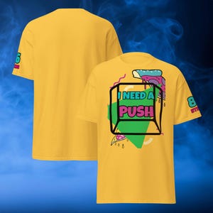 May include: Mustard yellow t-shirt with the text "I NEED A PUSH" inside a black outlined box. The shirt has a graphic design with a green triangle and a slice of pizza. The sleeve has the text "8 STYLES".