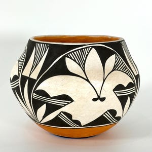 Könnte beinhalten: Eine handgefertigte Keramikschale mit runder Form. Die Schale hat ein schwarz-weißes geometrisches Design mit einem floralen Motiv. Der Rand und der Boden sind in Orange- und Brauntönen bemalt.