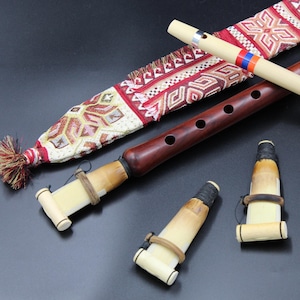 Puede incluir: Colección de flautas de madera y accesorios. Se ven dos flautas marrones, una flauta de color claro y dos boquillas. También hay una funda de tela estampada con borla. Las flautas tienen varios agujeros y longitudes variables.