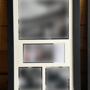 Puede incluir: Un marco de fotos negro con un paspartú blanco. El marco tiene una abertura grande y tres más pequeñas para mostrar fotos. El marco es de madera y tiene un acabado texturizado. El marco está diseñado para contener varias fotos.