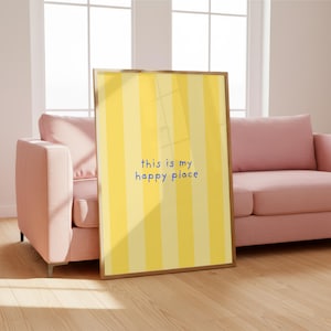 May include: A framed print with a yellow and cream striped design and the blue text "this is my happy place". The print is propped against a wooden floor, with a pink sofa and window visible in the background.