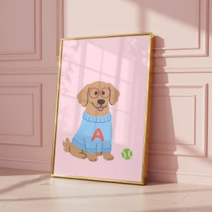 Könnte beinhalten: Gerahmte Illustration eines Cartoon-Hundes mit Brille und einem blauen Pullover mit dem Buchstaben "A". Ein grüner Tennisball liegt neben dem Hund auf rosa Hintergrund. Der Rahmen ist goldfarben.