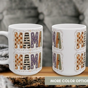 May include: Two white ceramic mugs featuring the word MAMA in large, patterned block letters. Each letter displays different designs including orange and white checkers, black and white stripes, purple with ghosts, and green with acorns.