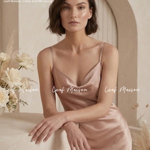 May include: A blush pink satin slip dress featuring a cowl neckline and thin spaghetti straps. The fabric has a smooth, reflective finish. The text Leaf Maison - Linen and Silk luxury and Leaf Maison appears on the image.