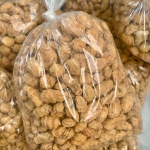 Puede incluir: Varias bolsas de plástico transparente llenas de chufas beige. Las bolsas están atadas en la parte superior con una brida. Las chufas son de color marrón claro y tienen una textura arrugada. Las bolsas están apiladas.