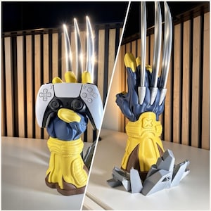 Puede incluir: Un soporte con forma de guantelete azul y amarillo que presenta tres largas garras plateadas metálicas que se extienden hacia arriba. El soporte sostiene un mando de juego blanco y negro y muestra una base gris de aspecto rocoso.