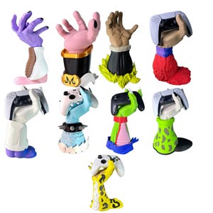 Op de afbeelding: Een collectie van negen handvormige controllerstandaards, elk met unieke kleurenschema's en texturen. Deze rechtopstaande figuren zijn ontworpen om gamecontrollers vast te houden en tonen diverse artistieke ontwerpen, waaronder paarse, roze, beige en groene handen.