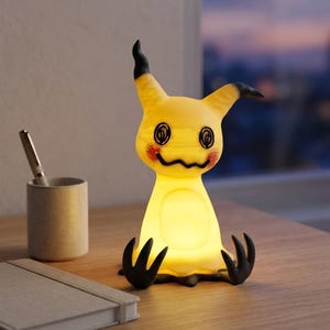 May include: A yellow, glowing lamp shaped like a creature with pointed ears, black tips, and scribbled facial features. The lamp has a rounded body, two black claw-like appendages at the base, and red circular markings on its cheeks.