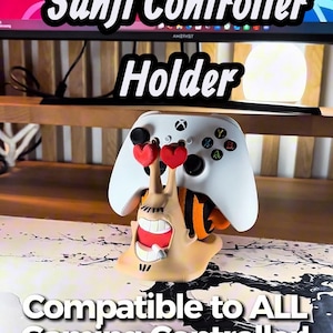 Op de afbeelding: Een beige slakvormige gaming controller houder met een personage met een sigaret in de mond en rode hartvormige ogen. De houder ondersteunt een witte Xbox-controller. De tekst op de afbeelding luidt Sanji Controller Holder en Compatible to ALL Gaming Controller!